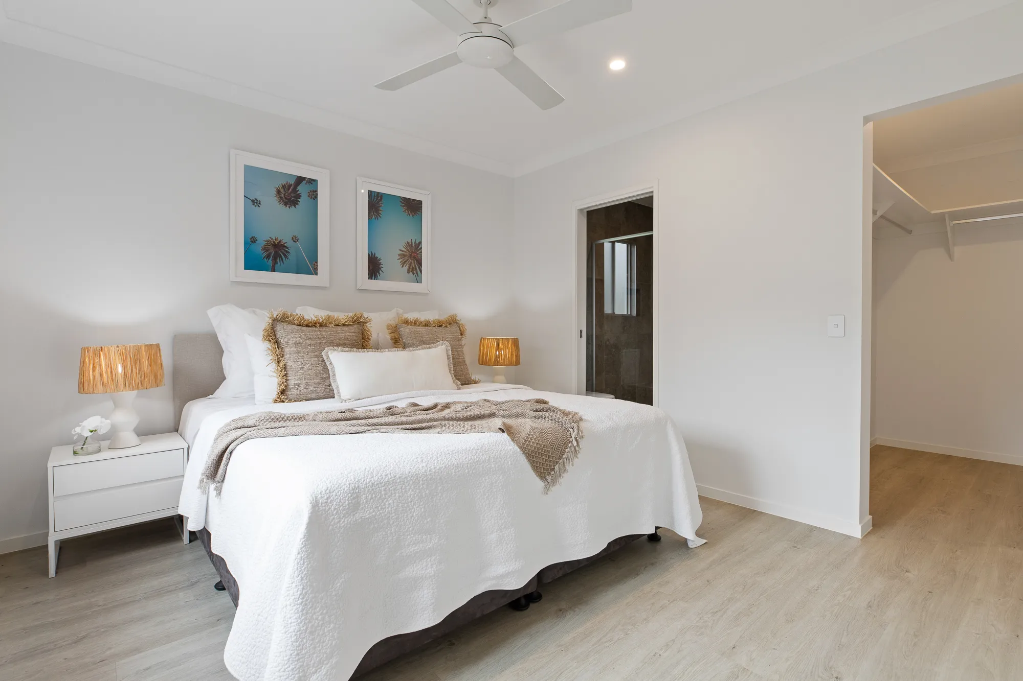 Painted bedroom interior with white walls and ceiling, a ceiling fan, framed prints above the bed and a walk-in robe.