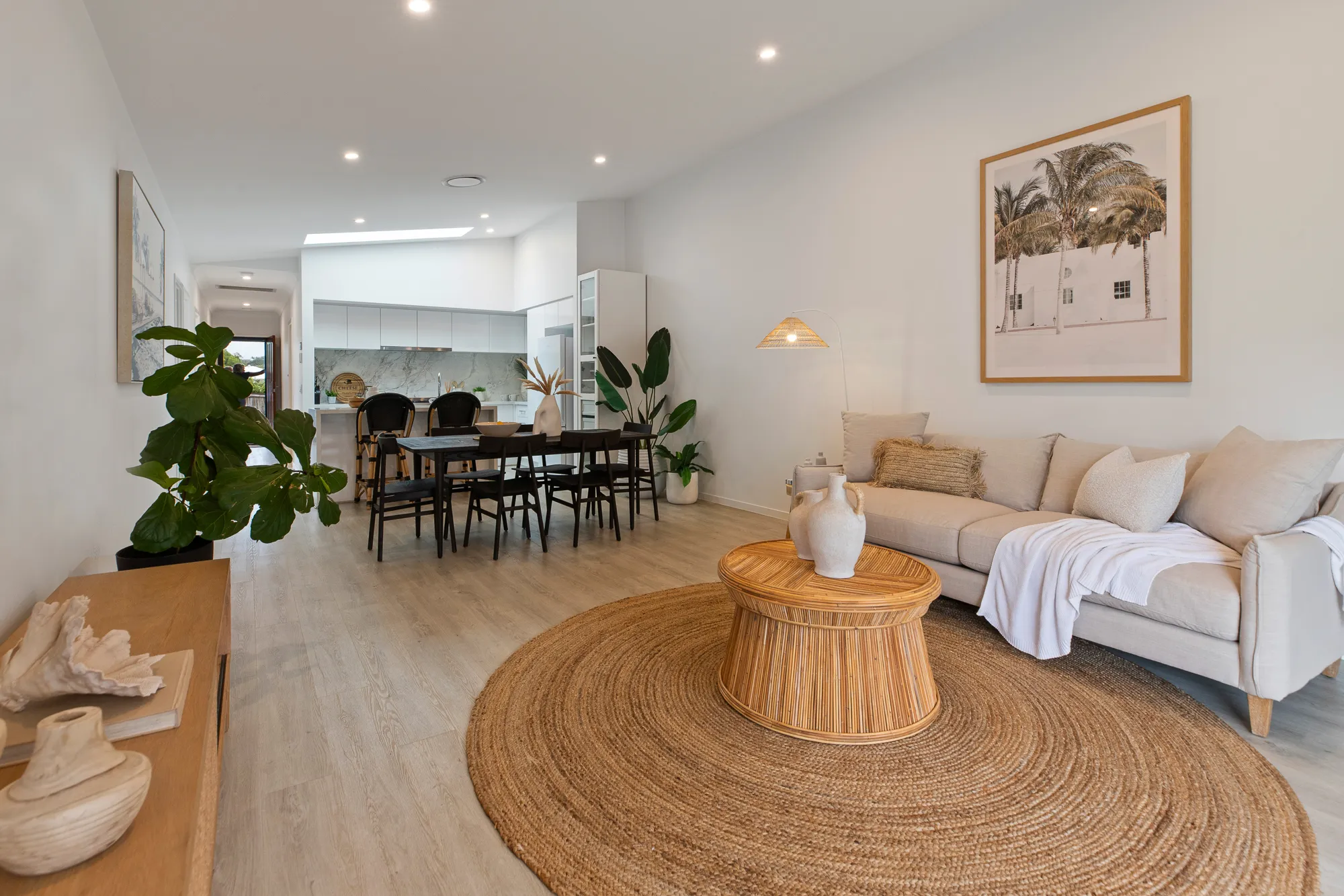Open-plan living, dining and kitchen with white walls and ceiling, timber floors, large windows and natural light, with coastal-style furnishings.